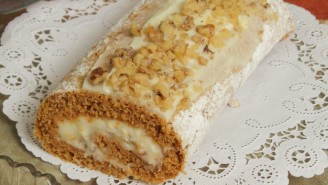A roll cake with white frosting and nuts on top.