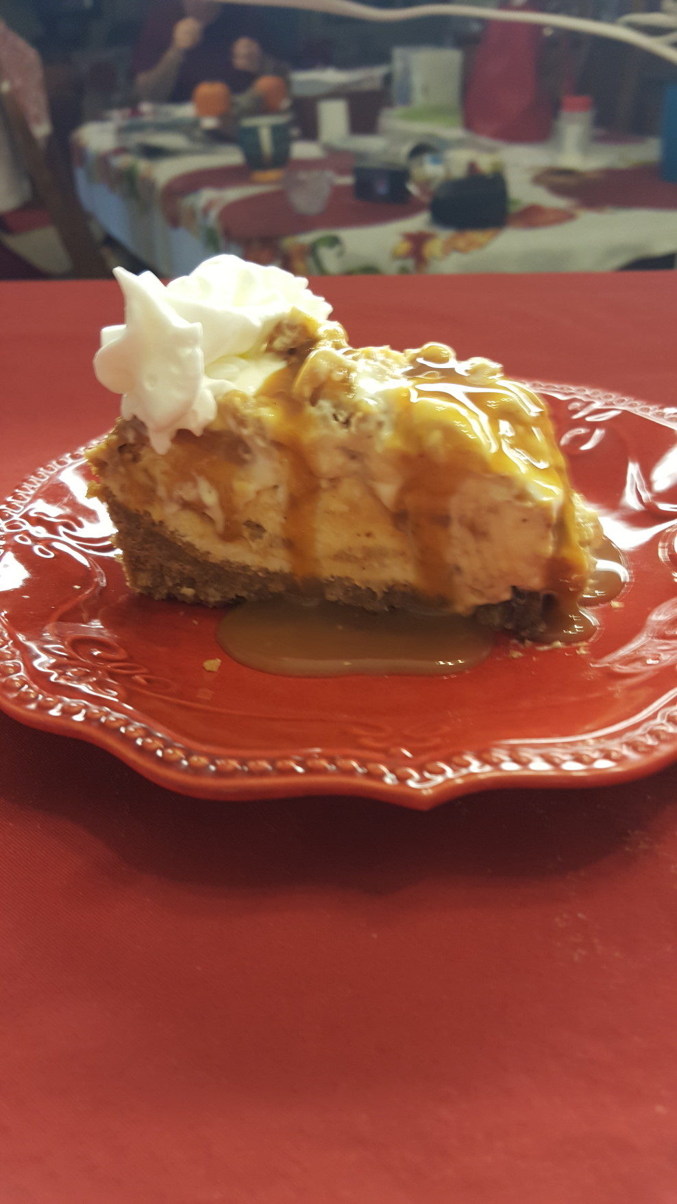 A red plate holding a piece of pie covered in whipped cream.