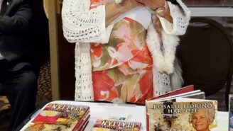 A woman holding a dog and standing next to a table with books.