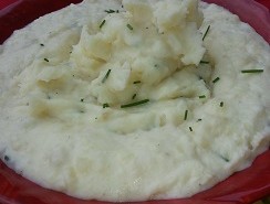 A bowl of mashed potatoes with chives on top.